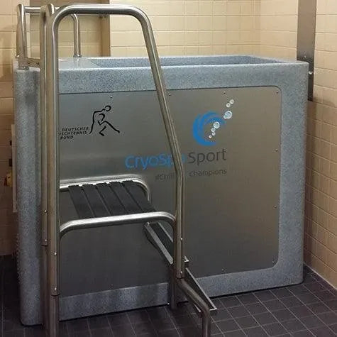 A cryotherapy chamber with a ladder for entry is placed in a tiled room. The chamber, designed specifically for athlete recovery, has a sign reading "CryoSpa Sport - Cold Water Ice Bath," along with a blue logo and bubbles. The German text "Deutsche Ski-Verband" with a skiing figure is also visible. The brand name "CET CryoSpas" can be seen as well.