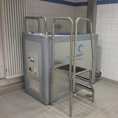 A metal cold plunge pool with a control panel and ladder in a tiled room. Designed for the CryoSpa Sport - Cold Water Ice Bath and athlete recovery, the pool features a robust cooling system and the logo "CET CryoSpas" on its side. A wall-mounted radiator is visible in the background, perfect for ice bath therapy sessions.