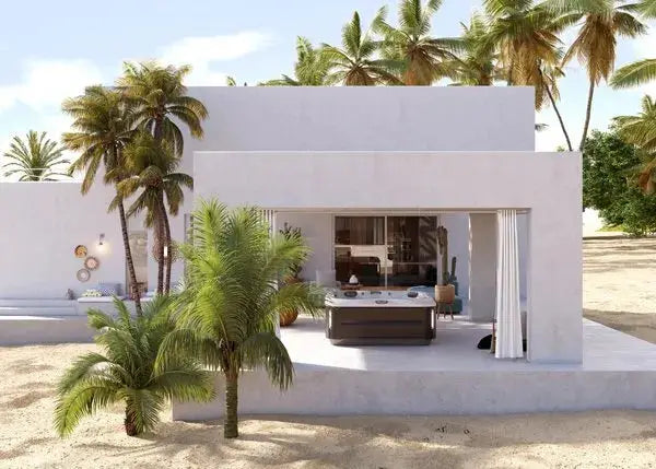 A modern, minimalist beachfront house with white exterior walls and large windows. The open patio area features a Jacuzzi® J-335 COMFORT HOT TUB WITH OPEN SEATING and lounge chairs. Surrounding the house are tall palm trees and a sandy beach, creating a serene, tropical setting.