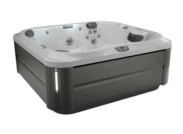 A modern Jacuzzi J-355 HOT TUB WITH COMFORT LOUNGE SEATING & COOL DOWN SEAT with gray exterior panels and a white interior. It features multiple built-in hydrotherapy jets, a digital control panel, and cushioned headrests in each corner. The hot tub is designed to accommodate several people for an ultimate relaxation experience.