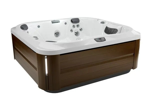 A square Jacuzzi J-355 HOT TUB WITH COMFORT LOUNGE SEATING & COOL DOWN SEAT with a white interior and a brown wooden exterior is shown. It features multiple hydrotherapy jets, a headrest, and a small control panel. The hot tub has rounded corners, a sleek modern design, and includes the ProClear filtration system for crystal-clear water.