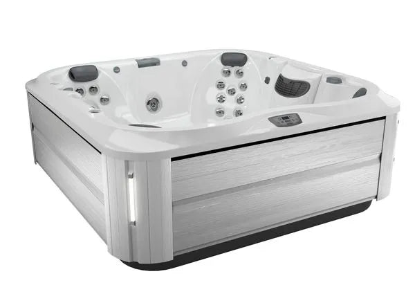 A white, rectangular J-375 COMFORT HOT TUB WITH LARGEST LOUNGE SEAT NEW by Jacuzzi with gray wooden paneling designed for indoor and outdoor installation. The hot tub features multiple seats, jets, advanced hydromassage technology, and a control panel for settings adjustment. The exterior boasts a sleek, modern design.