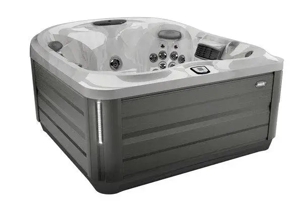 A rectangular, modern hot tub with a sleek design featuring Jacuzzi PowerPro jets for exceptional hydrotherapy. The J-445™ OPEN SEATED HOT TUB WITH INFRARED & RED LIGHT THERAPY by Jacuzzi has multiple seating areas and a grey exterior with a marble-patterned interior. The control panel is visible on the side, along with LED lights and speaker grills.