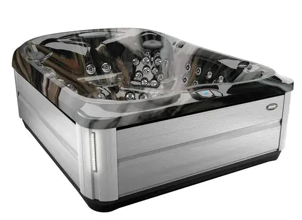 A large, luxurious Jacuzzi J-495™ DESIGNER ENTERTAINER'S HOT TUB WITH INFRARED & RED LIGHT THERAPY - NEW MODEL with multiple PowerPro jets. The hot tub has a sleek, modern design with a dark, marble-patterned interior and a silver exterior. It features various seating positions and built-in controls on the rim for an unparalleled hydromassage experience.