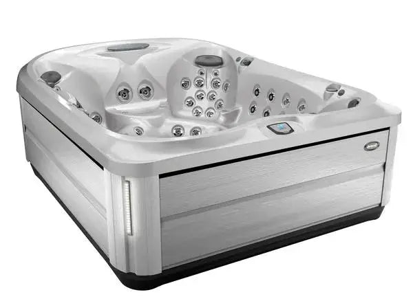 A modern, white Jacuzzi J-495™ DESIGNER ENTERTAINER'S HOT TUB WITH INFRARED & RED LIGHT THERAPY - NEW MODEL is shown. It has a sleek design with textured exterior siding and an integrated control panel. The corners are rounded, and the overall aesthetic is contemporary and luxurious, promising a premium hydromassage experience.