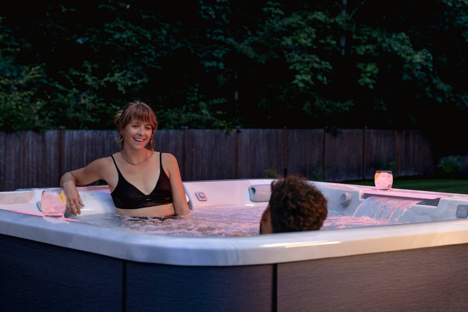 Two people in a hot tub at night with trees in the background