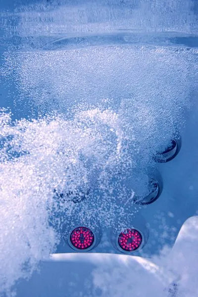 Close-up of a Jacuzzi - J-LXL Hot Tub's water jets in action, creating bubbles and turbulence. Two underwater lights illuminate the water with a soft, red glow, enhancing the swirling, foamy water. The scene has a soothing and invigorating vibe, emphasizing relaxation through hydrotherapy.