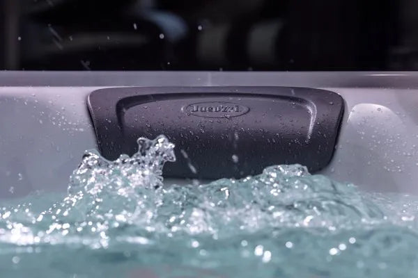 A close-up of a Jacuzzi - J-LXL Hot Tub filled with bubbling water. The image shows the water's surface churning and splashing near a cushioned headrest labeled 