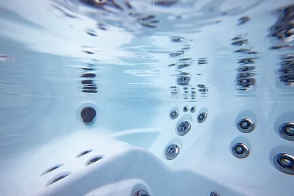 Underwater view of a Jacuzzi - J-LXL Hot Tub showing its numerous jet outlets and the clear, bubbling water surface above. The perspective highlights the sleek design and placement of the jets around the inner walls of the tub, providing optimal hydrotherapy benefits for ultimate relaxation.