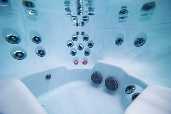 Underwater view of an empty **Jacuzzi - J-LXL Hot Tub** featuring multiple massage jets on its walls and seats. The interior is clean and bright with reflective surfaces, and two circular speakers are visible near a seat. Two glowing pink lights, perfect for hydrotherapy, are positioned above the speakers.

