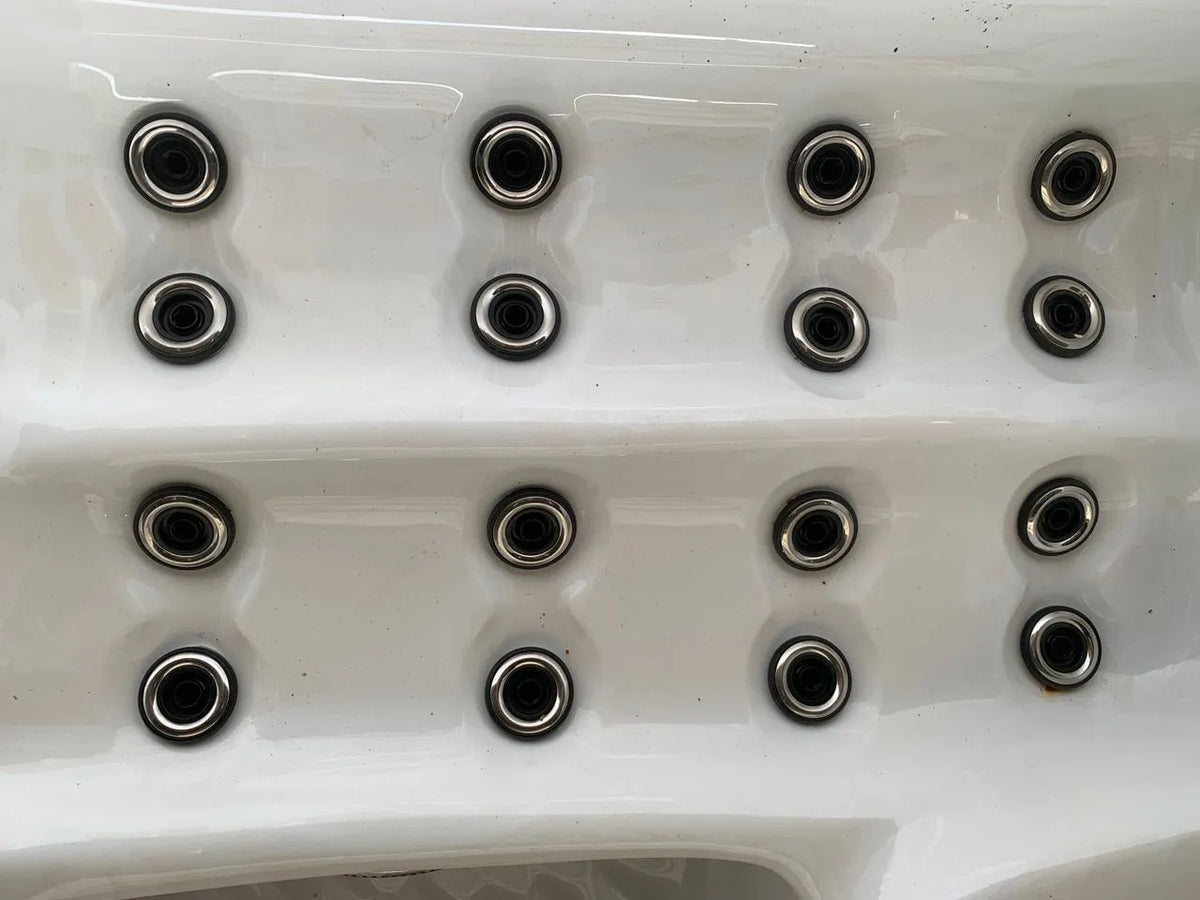 A close-up image of a white surface with multiple small, circular holes arranged in a grid pattern. Each hole is encircled by metal rings, reminiscent of the Atlanta - 2-3 Person Hot Tub by Hot Tub Liverpool, giving the appearance of an industrial component.