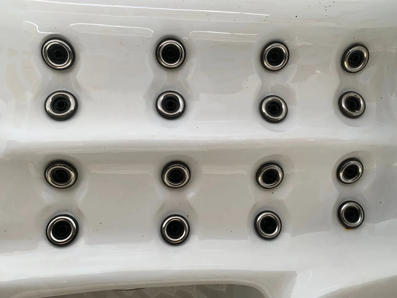 A close-up image of a white surface with multiple small, circular holes arranged in a grid pattern. Each hole is encircled by metal rings, reminiscent of the Atlanta - 2-3 Person Hot Tub by Hot Tub Liverpool, giving the appearance of an industrial component.