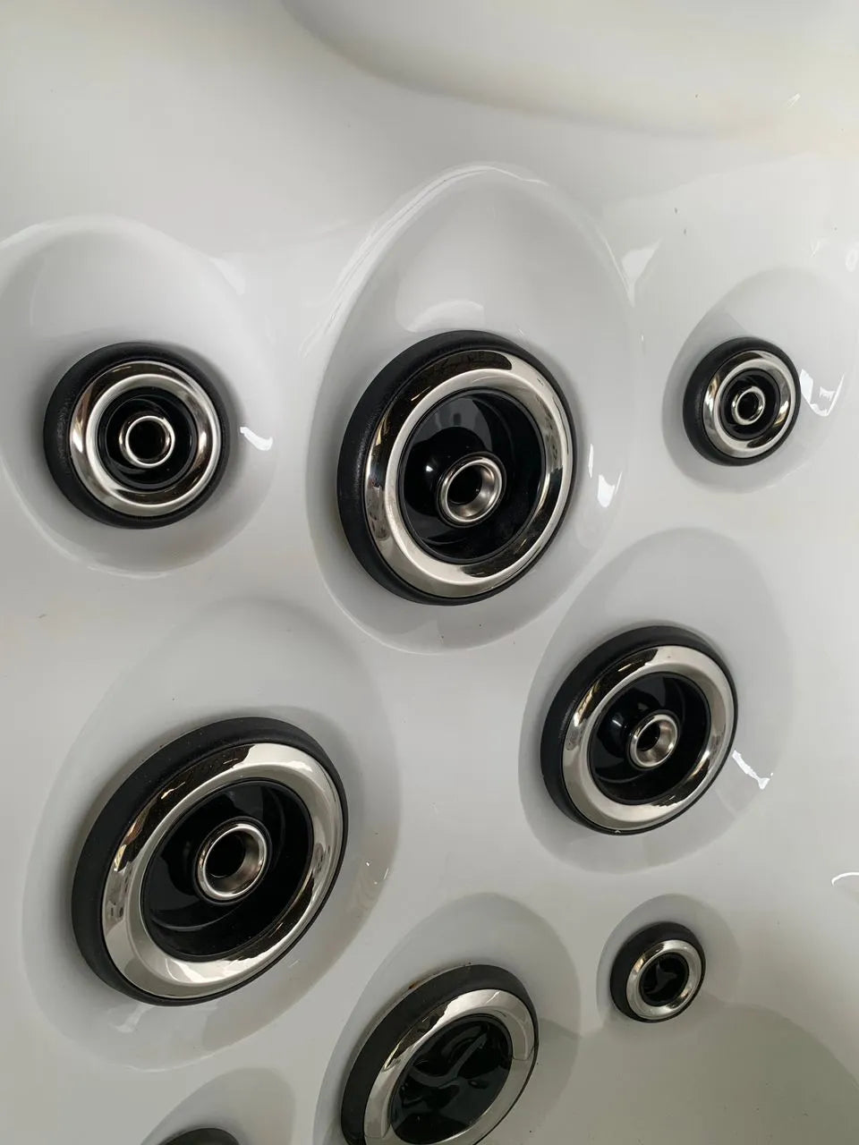 Close-up view of black and silver circular jets installed in a white jacuzzi tub. The jets, part of the Balboa Control System, are embedded in a pattern to provide hydrotherapy and a massage-like experience. The smooth, glossy surface of the Hot Tub Liverpool Atlanta - 2-3 Person Hot Tub is visible around the customizable jets.