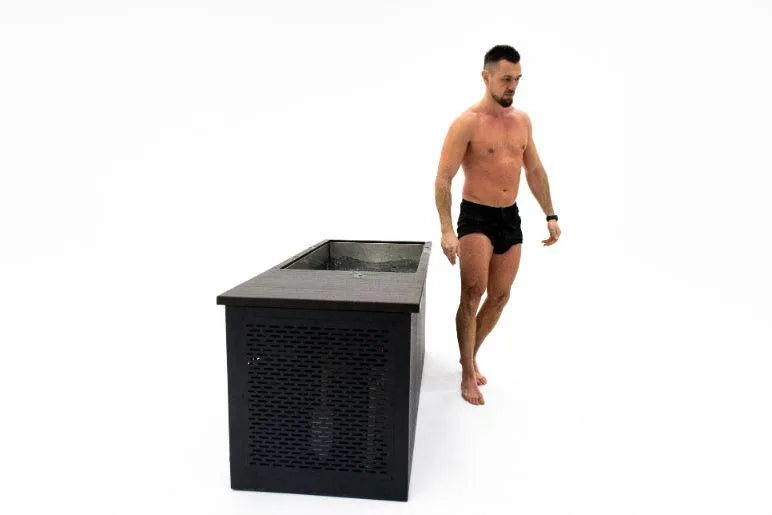 A man in black shorts and no shirt stands next to a large rectangular container, possibly a Chill Tubs - Professional affordable Ice Baths ideal for gym fanatics by Chill Tubs, against a white background. He appears poised and ready to enter the container for cold water therapy.