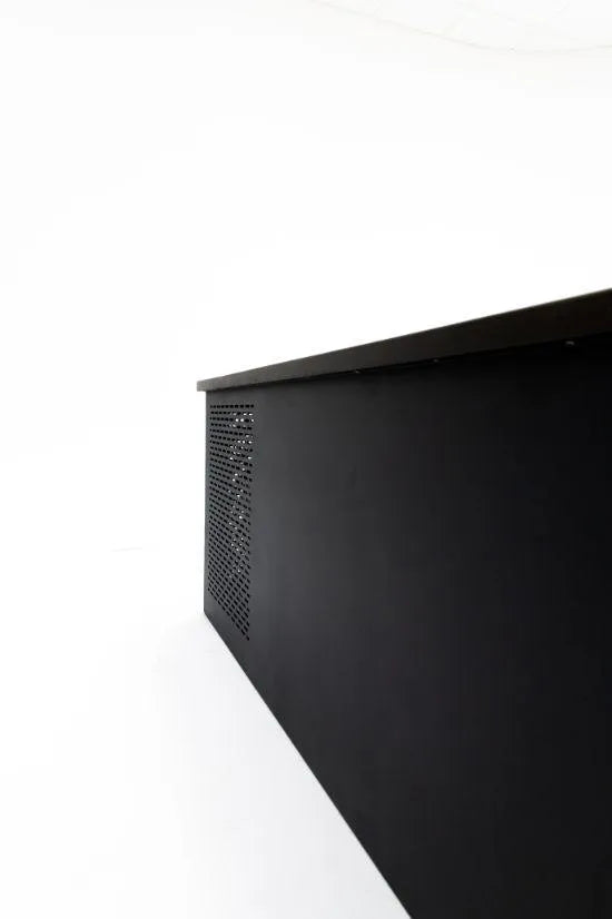 A minimalist photograph featuring a black desk or table set against a stark white background. The angle shows the bottom and side of the desk, which has a perforated design element on one side. The clean and modern aesthetic evokes the tranquil simplicity of Chill Tubs - Professional affordable Ice Baths ideal for gym fanatics used in cold water therapy by Chill Tubs.
