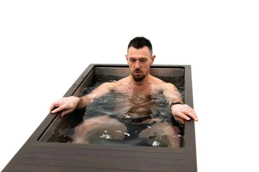 A man with short dark hair and a beard sits in a Chill Tubs - Professional affordable Ice Baths ideal for gym fanatics with water up to his chest, arms resting on the sides of the tub. The background is plain white. He appears relaxed yet focused, embracing the benefits of cold water therapy.