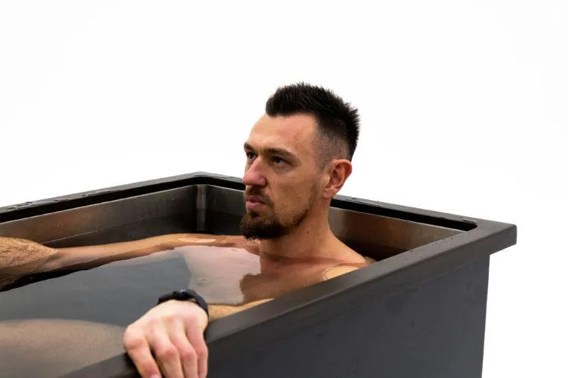 A man with short dark hair and a goatee is sitting in a large black Chill Tubs - Professional affordable Ice Baths ideal for gym fanatics, partaking in cold water therapy. He is looking to the side and resting one arm on the edge of the Chill Tubs container. The background is plain white.