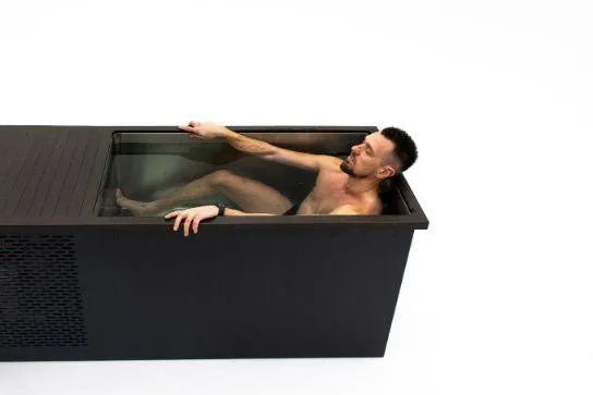 A man with short hair, wearing a wristwatch, relaxes in a black Chill Tubs - Professional affordable Ice Baths ideal for gym fanatics filled with water. He is lying back with his eyes closed, partially submerged. The Chill Tubs tank is set against a plain white background.