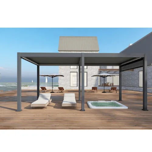 Outdoor patio with two modern design Jacuzzi® Pergola 3600 shading two lounge chairs each, featuring motorised louvre roofs and subtle LED strips. A hot tub is on the wooden deck in the foreground, and the beach is visible in the background. The house boasts large windows and light gray stone walls under a clear blue sky.