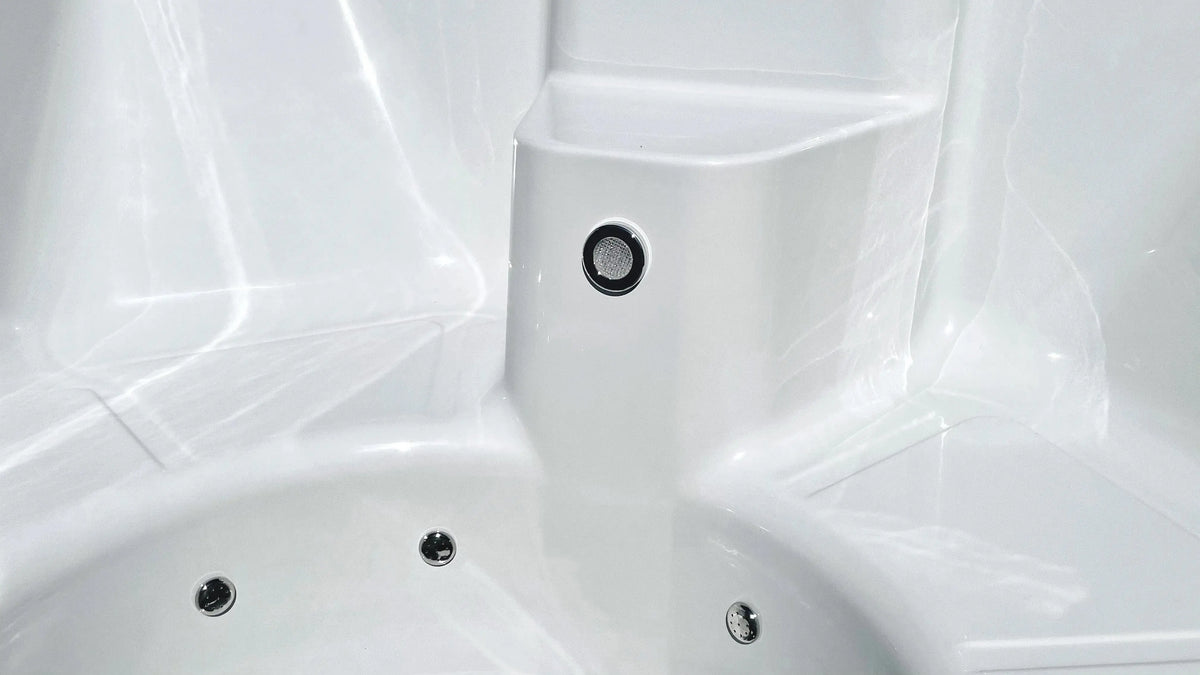 Close-up of a white, empty jacuzzi with circular jets visible. The smooth, glossy surface of the fibreglass pool reflects light. A small button or nozzle is seen on a raised section above the main tub area, suggestive of a well-designed handmade Rexener Polar Wooden Hot Tub - Made in Finland by Hot Tub Liverpool.