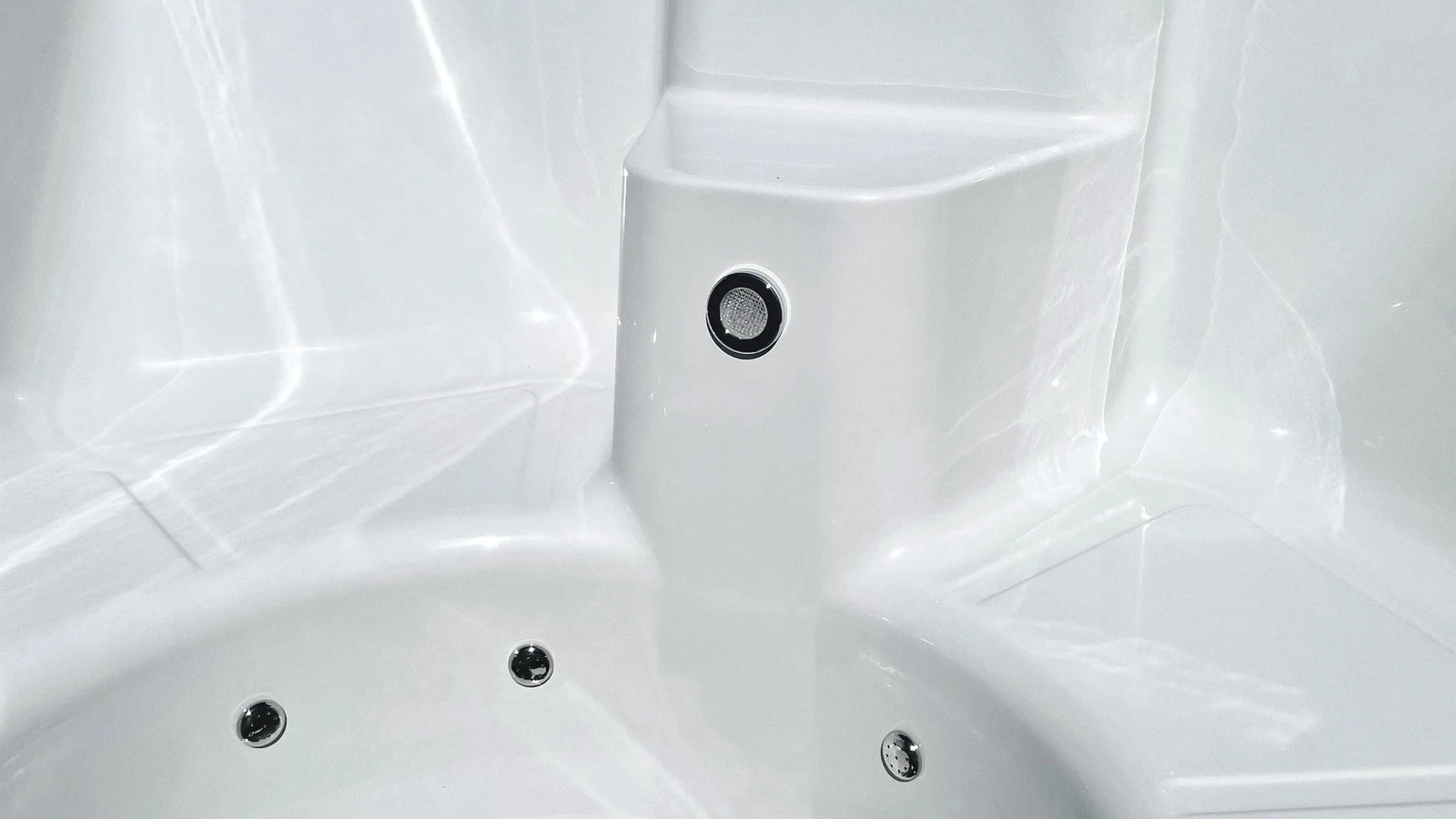 Close-up of a white, empty jacuzzi with circular jets visible. The smooth, glossy surface of the fibreglass pool reflects light. A small button or nozzle is seen on a raised section above the main tub area, suggestive of a well-designed handmade Rexener Polar Wooden Hot Tub - Made in Finland by Hot Tub Liverpool.