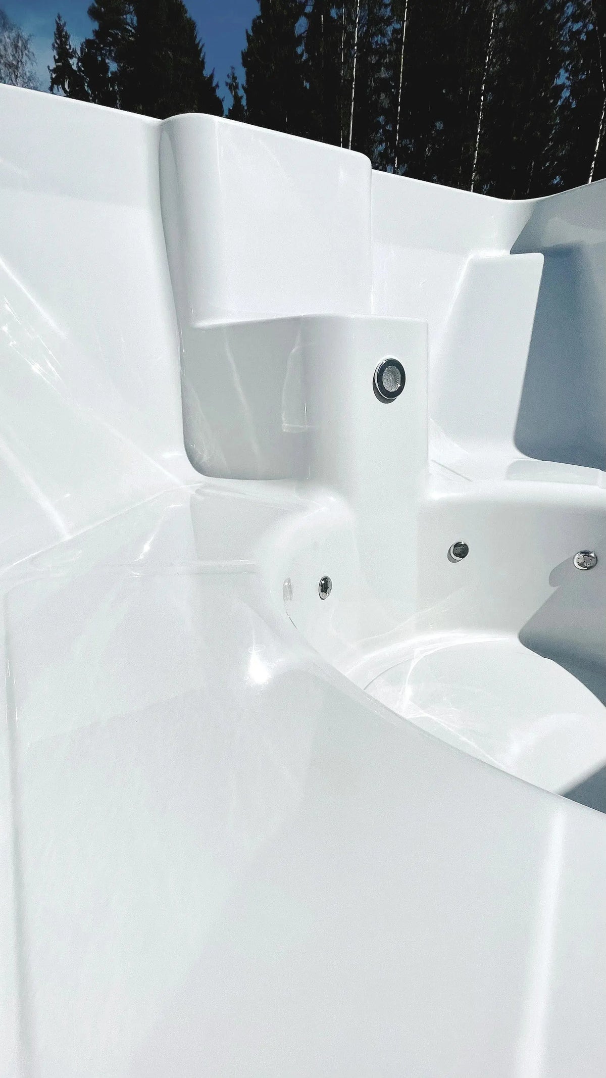 A gleaming white handmade hot tub, empty and clean, sits under bright sunlight. The surrounding area features lush green trees, creating a serene and inviting atmosphere for relaxation. Equipped with a Hot Tub Liverpool Rexener Polar Wooden Hot Tub - Made in Finland water heater, the hot tub has multiple seating areas and jet outlets.
