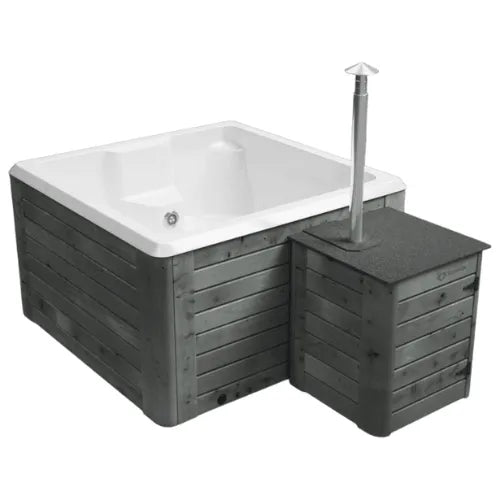 A square, handmade hot tub with a wooden exterior and a white interior. Attached to the side is a small, box-like compartment with a stovepipe extending from the top, indicating a wood-fired heating mechanism. This is the Rexener Polar Wooden Hot Tub - Made in Finland by Hot Tub Liverpool.