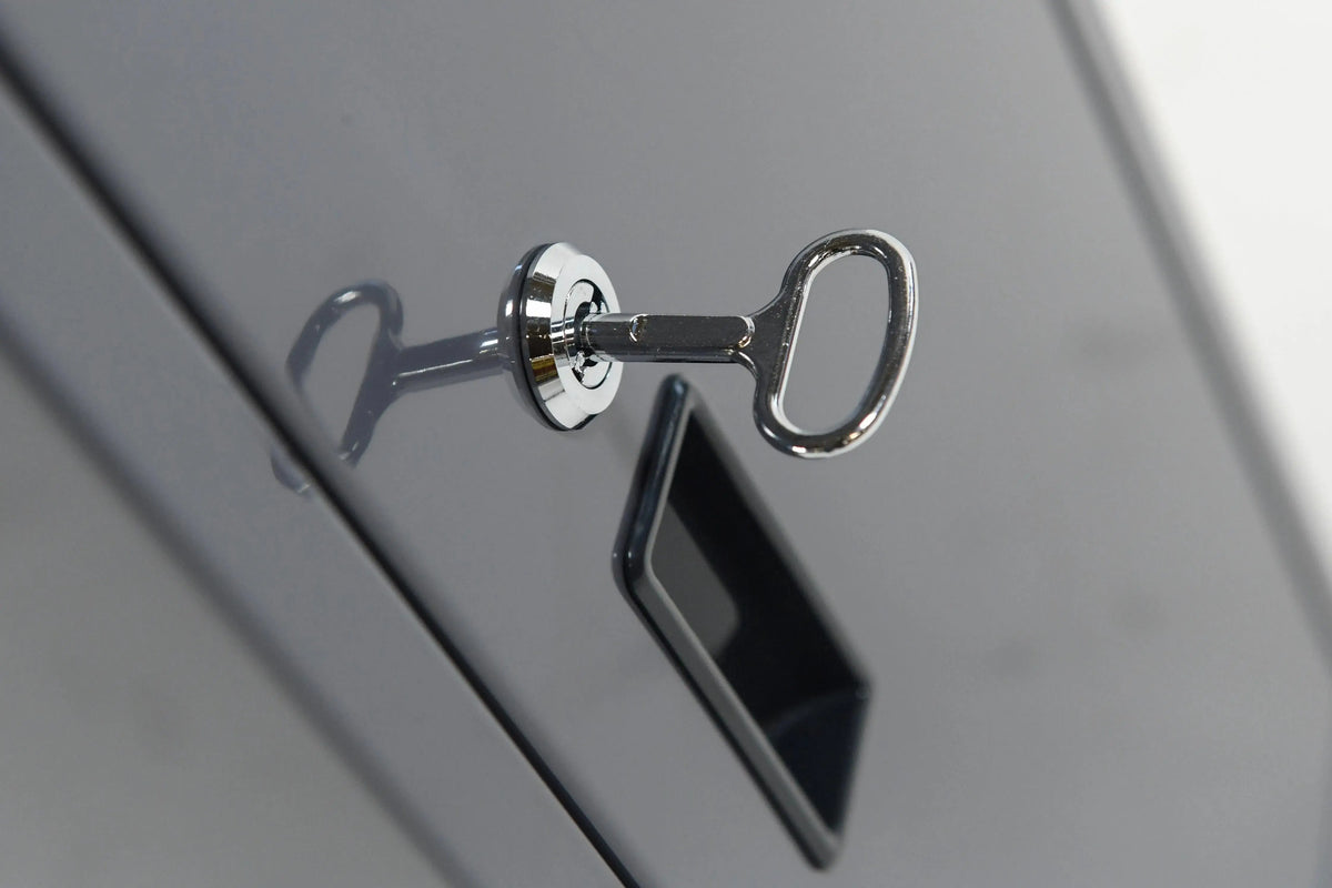 A close-up image of a silver key inserted into a lock of a metallic gray filing cabinet's drawer. The key has a rounded head, and the reflection of the key is visible on the glossy surface of the cabinet, perfect for storing manuals for Hot Tub Liverpool's REXENER PR200 energy efficient hot tub water heater.