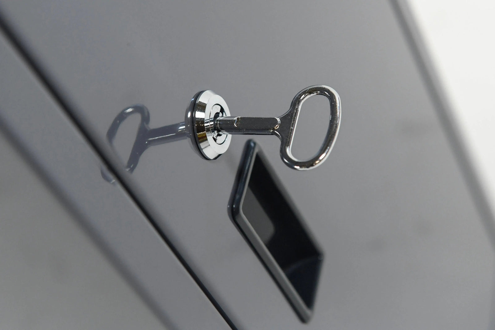 A close-up image of a silver key inserted into a lock of a metallic gray filing cabinet's drawer. The key has a rounded head, and the reflection of the key is visible on the glossy surface of the cabinet, perfect for storing manuals for Hot Tub Liverpool's REXENER PR200 energy efficient hot tub water heater.