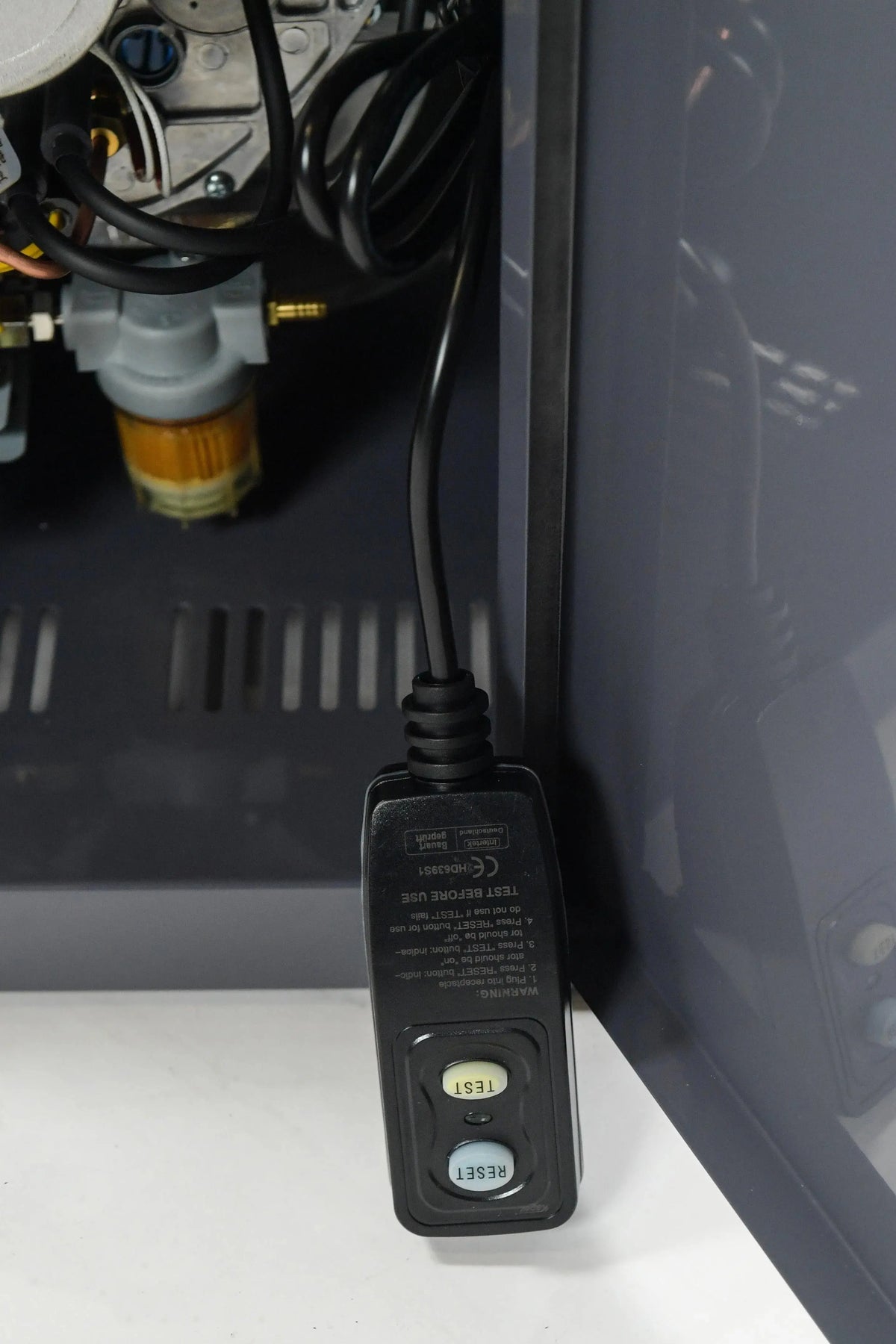 Close-up of a ground fault circuit interrupter (GFCI) outlet within an electrical setup for the Hot Tub Liverpool REXENER PR200 energy efficient hot tub water heater, featuring a black housing with a label indicating "Test Before Use." The outlet has two buttons: a yellow "Test" button and a blue "Reset" button.