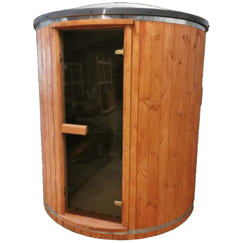 A cylindrical wooden Sunbeach Spas Woodpecker 2M Tube Outdoor Sauna (Pre-Built) with a glass door, featuring horizontal wood paneling and a metal band around the top and bottom edges. The sauna, equipped with an electric heater, stands in an indoor space with various tools and equipment visible in the background.
