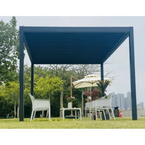 A modern outdoor patio setup with a Sunbeach Spas Sunhut Manual Pergoda (3M x 3M) featuring adjustable slats for customizable shade. Underneath, there are white chairs and tables with decor, and an umbrella. The background shows green trees, a river, and distant city buildings against a clear sky.