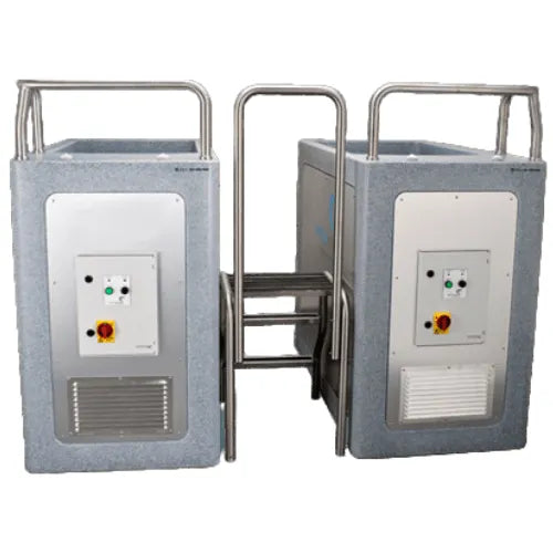 A pair of industrial-looking, large gray Team CryoSpa Sport Ice Bath machines from CET CryoSpas with control panels on the front, featuring green and red buttons. They are separated by a central metallic bar with handlebars on both sides. The machines have a sturdy, utilitarian design and appear to be interconnected for athlete recovery.